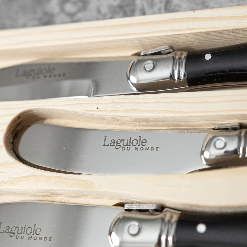 Close-up of the Laguiole Du Monde cheese knives with black handles in their wooden box